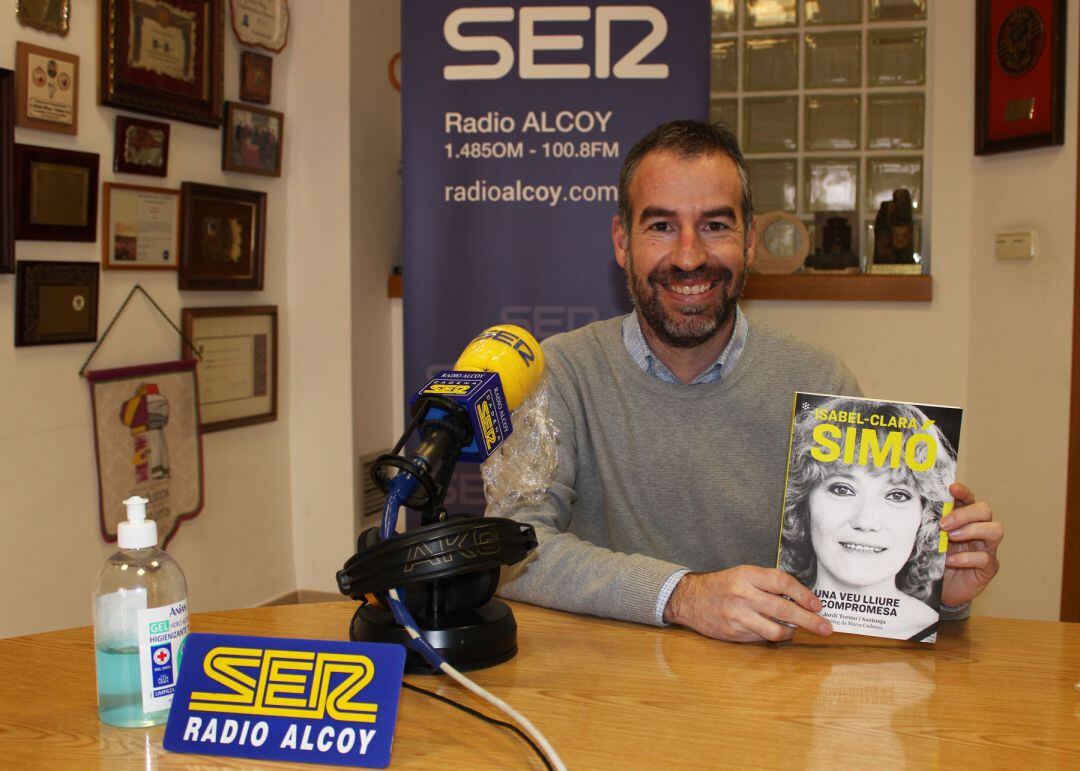 Jordi Tormo mostra en els estudis de Radio Alcoy un exemplar del llibre 'Isabel-Clara Simó, una veu lliure i compromesa'