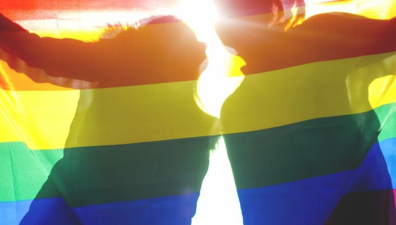 Dos personas detrás de una bandera arco iris.