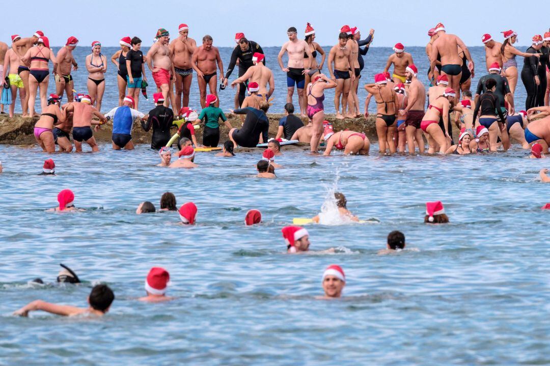 Un centenar de bañistas ataviados como Papá Noel han cruzado hoy desde la orilla de la playa de Las Canteras,hasta La Barra.