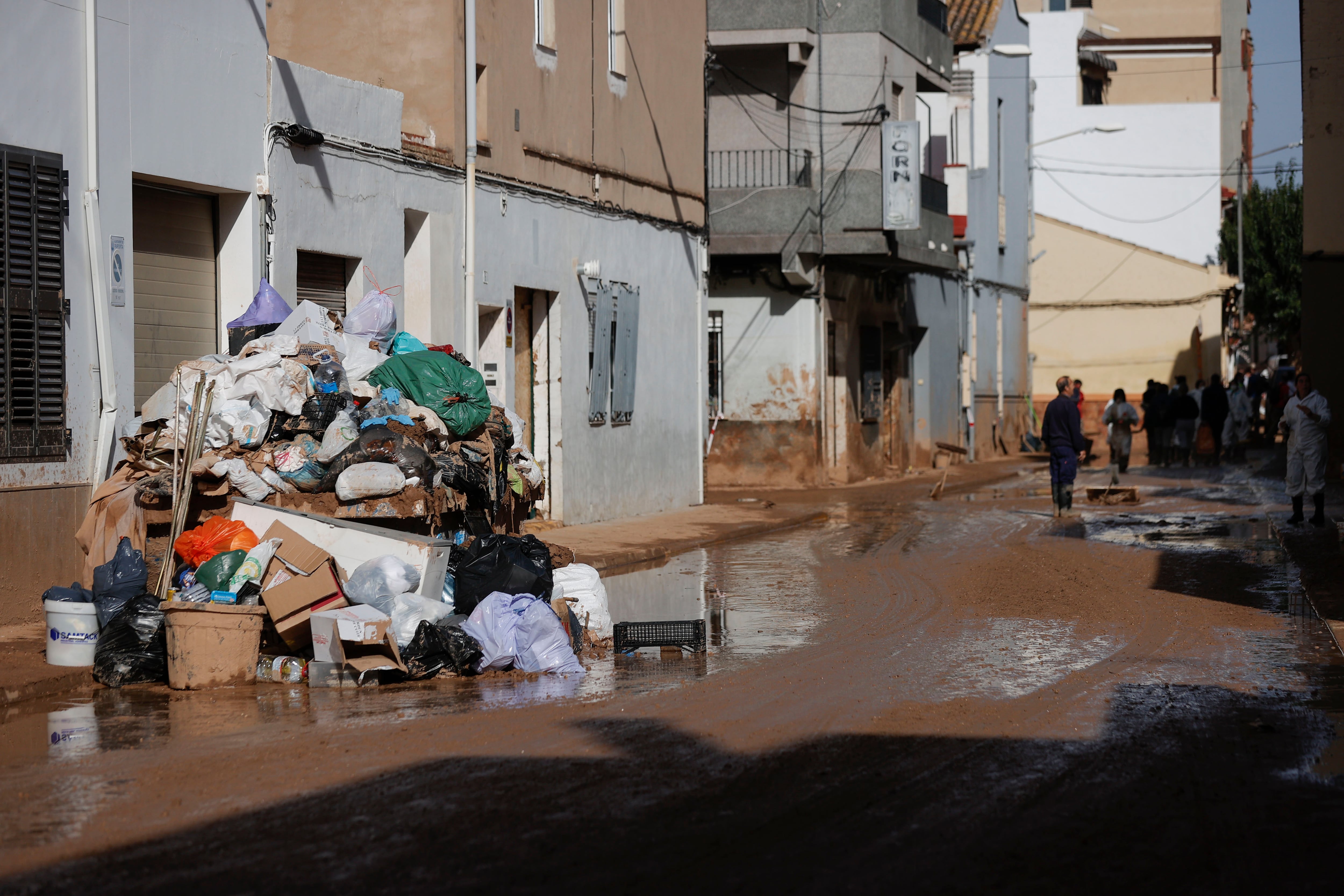 Enseres y bolsas de basura en una calle que continúa cubierta de barro en Paiporta.