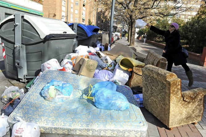 Una mujer se dispone a depositar una bolsa de basura junto a varios contenedores que acumulan gran cantidad de residuos, en una calle del centro de Granada