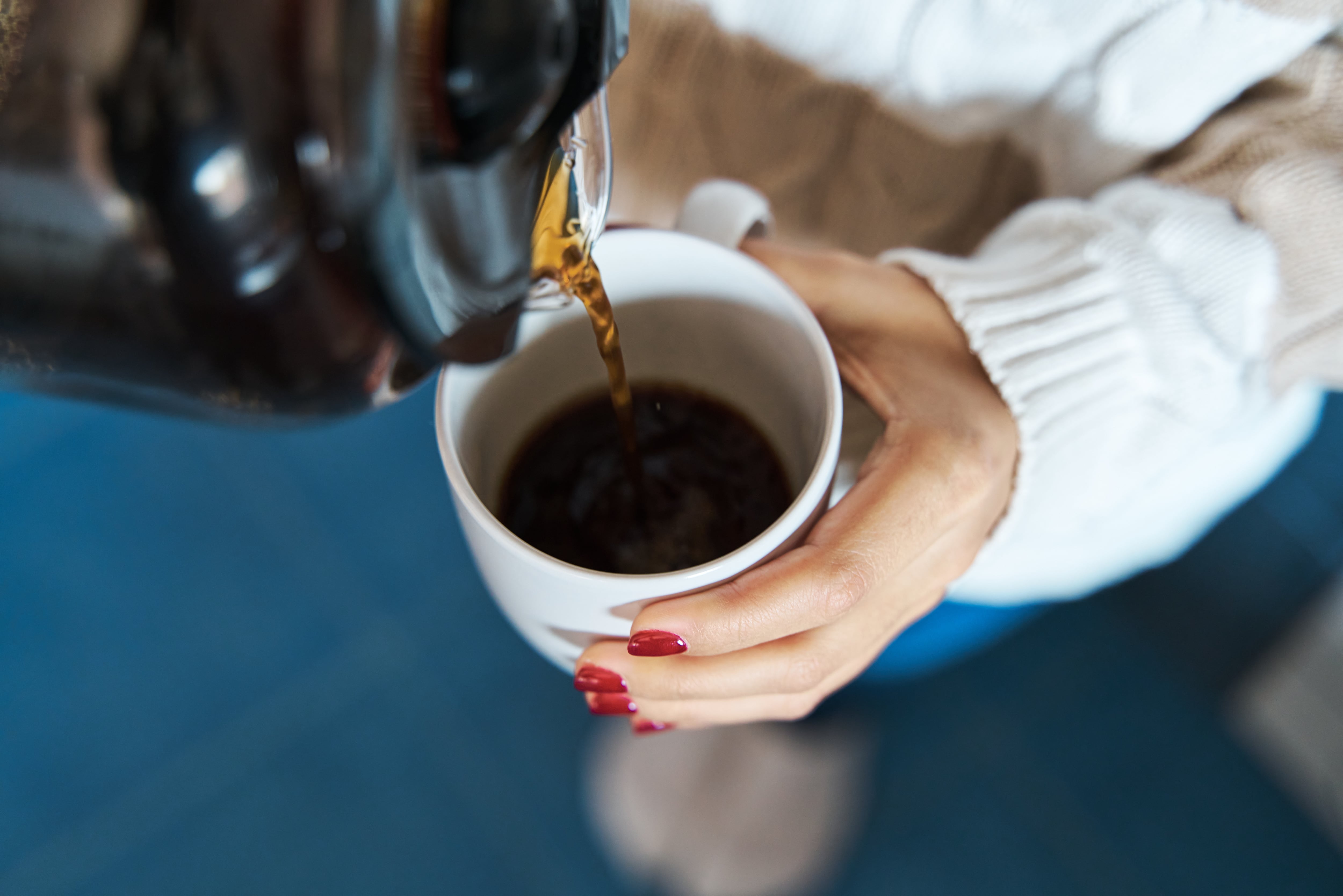 Un mujer sirviéndose café de cafetera en una taza.