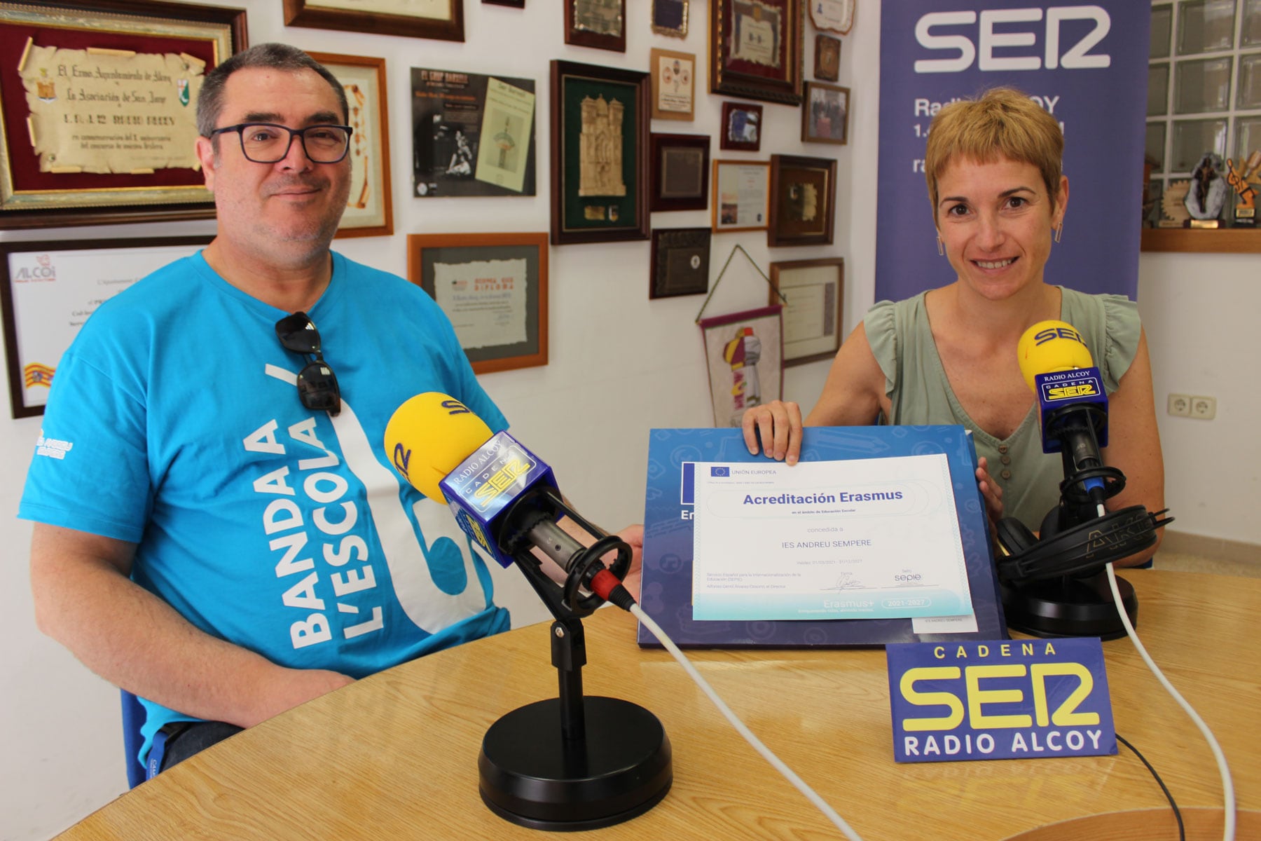El director Jesús Martínez, con la camiseta de la Banda a l'Escola, y la profesora Inma Bononat, sosteniendo el certificado de acreditación como centro Erasmus 2021-27