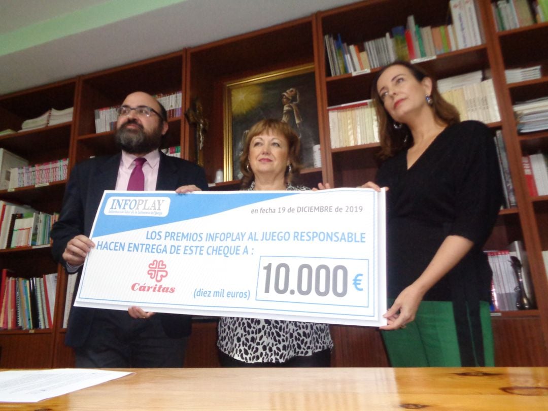 La presidenta de Cáritas recibe este cheque de la directora de Infojuego, acompañada de Máximo López