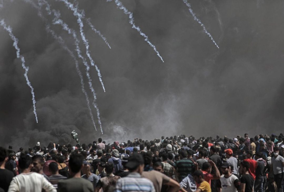 Varios manifestantes palestinos ante un muro de gas lacrimógeno