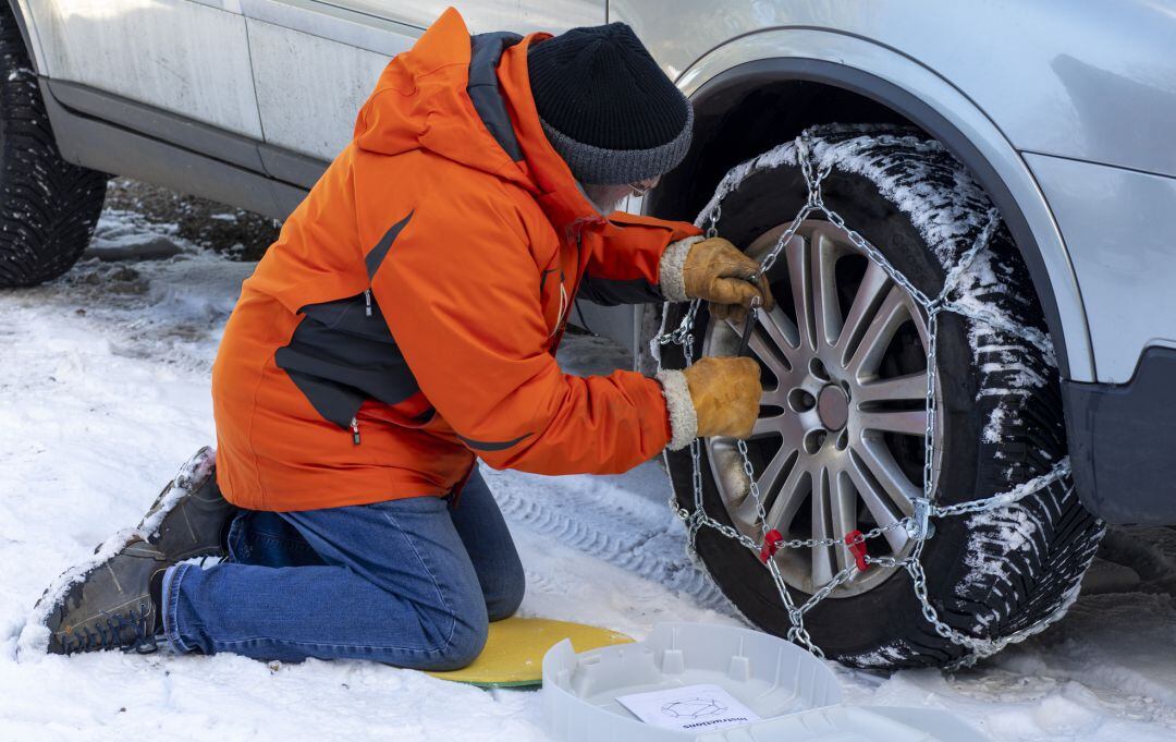 Una persona pone las cadenas de nieve en la rueda del coche.