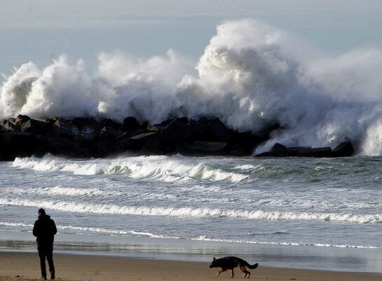 Un hombre pasea a su perro en la playa de La Zurriola de San Sebastián, donde el temporal ha dejado grandes olas