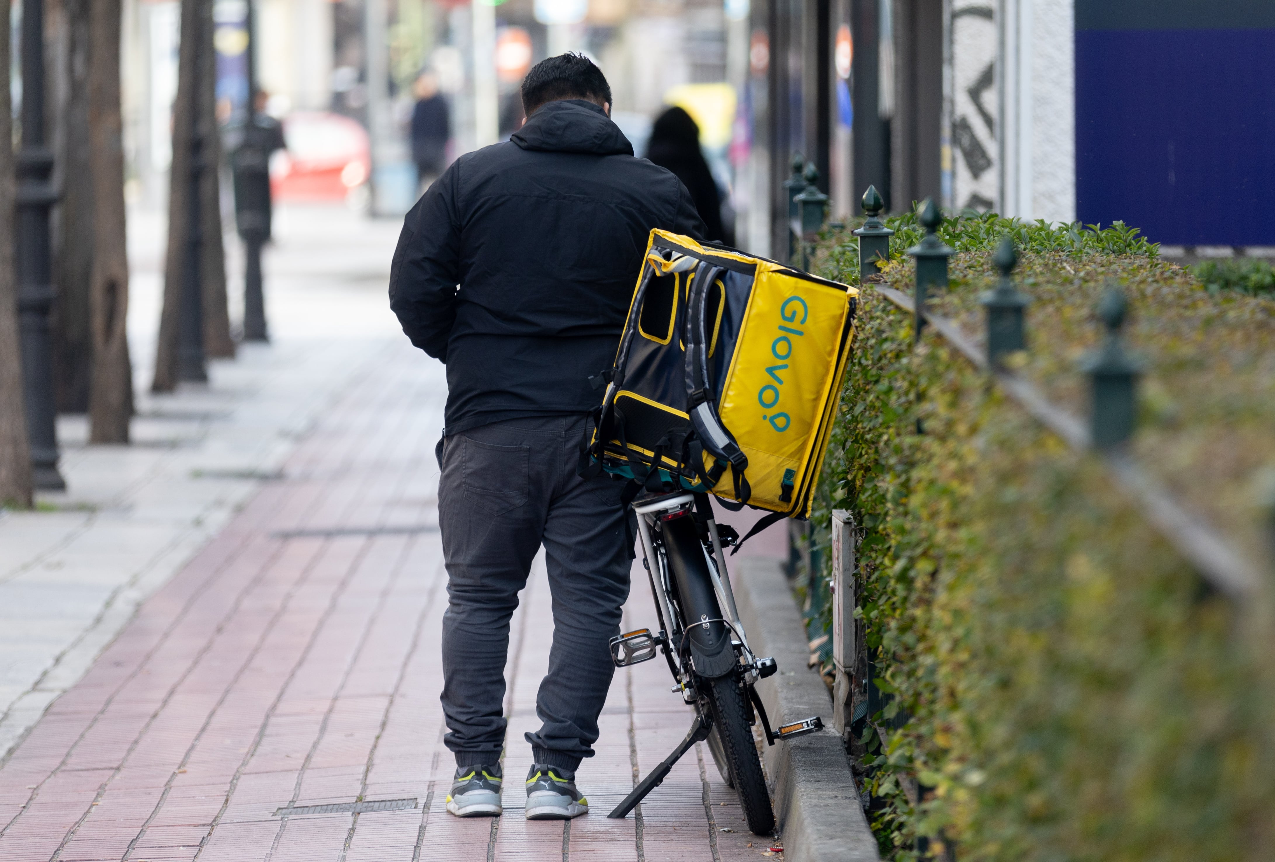 Un repartidor de Glovo esperant al costat de la seva bicicleta.