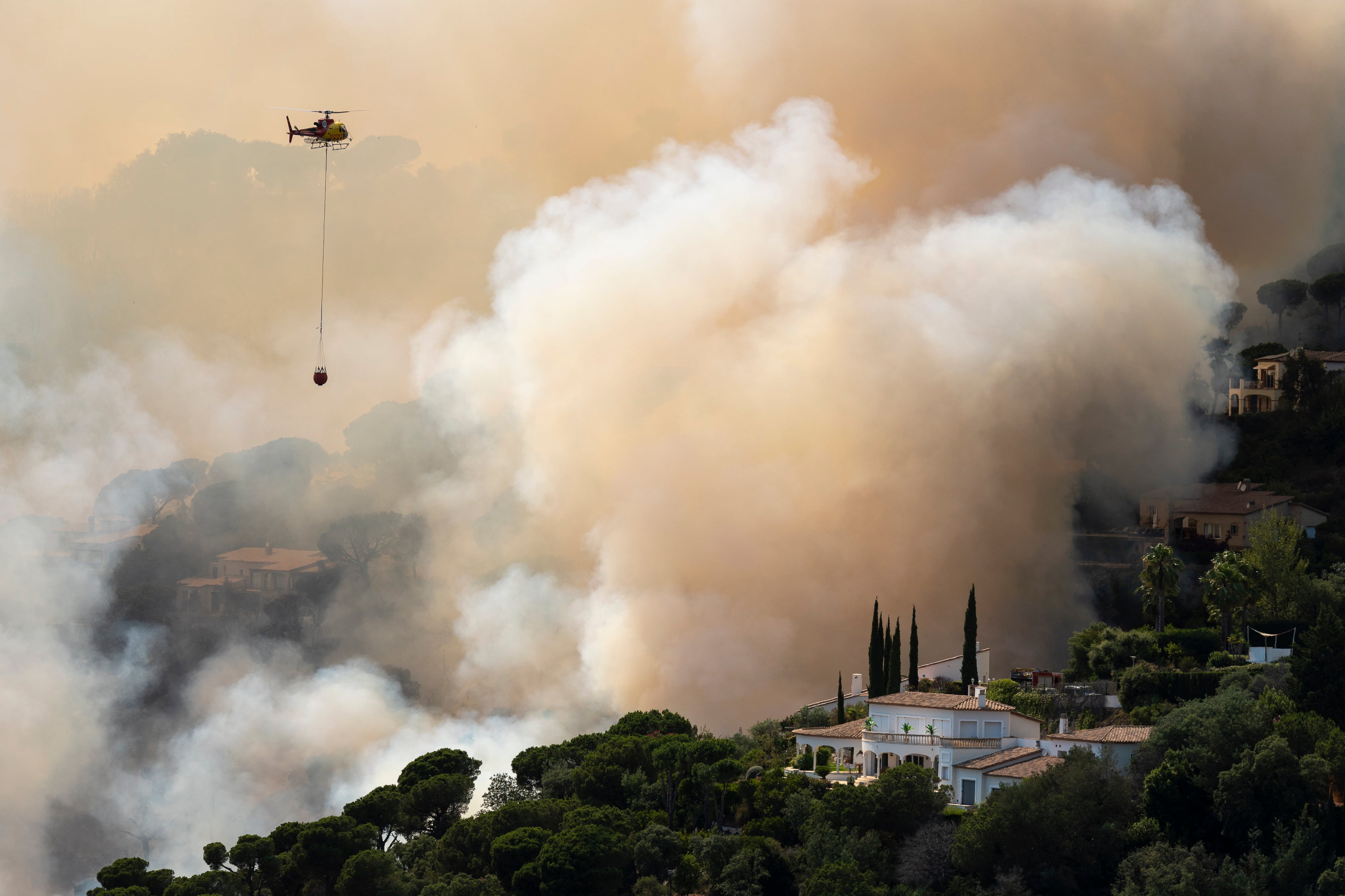 Un helicóptero trata de sofocar las llamas de un incendio forestal en la localidad de Santa Cristina d&#039;Aro