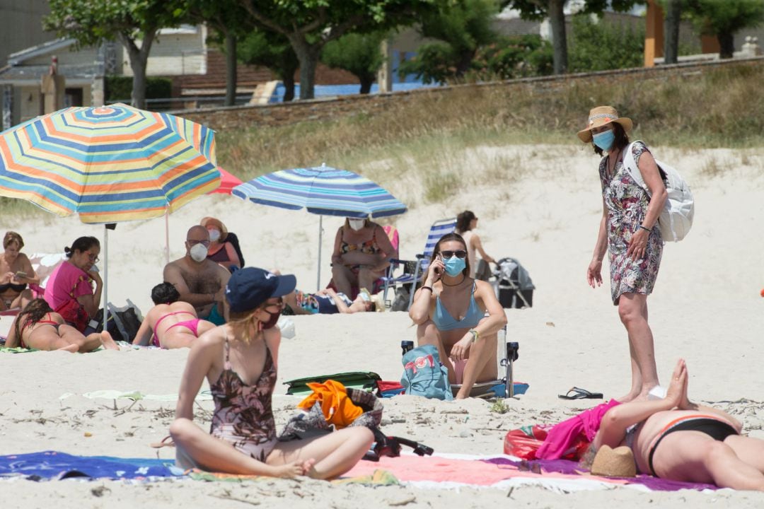 Varias personas protegidas con mascarillas toman el sol en la playa de A Rapadoira en Foz, en la comarca de A Mariña, Lugo,