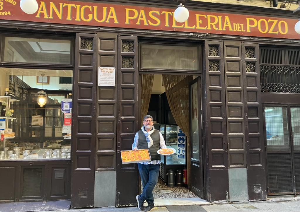 Antonio Pérez, encargado de La Antigua Pastelería del del Pozo, el jueves santo sujetando dos de los postres más populares de su local: las torrijas y las monas de pascua. / LAURA ÁLVAREZ