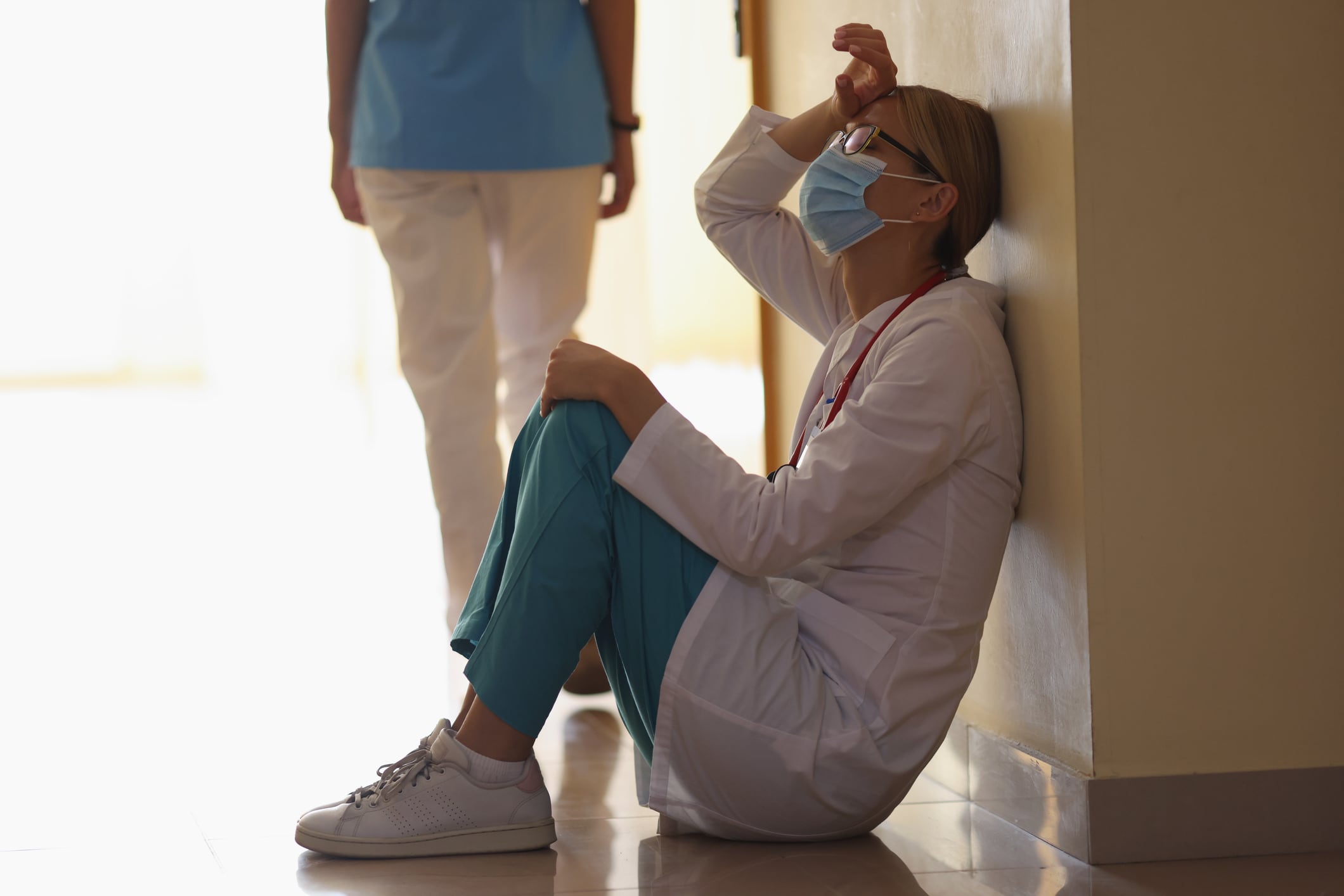 Una médico se echa la mano a la frente sentada en el suelo de un Hospital.