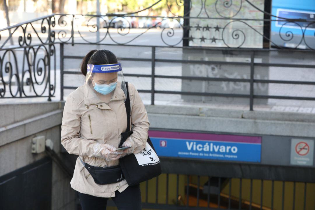 Una mujer protegida con mascarilla y pantalla protectora espera en la entrada al metro de Vicálvaro, Madrid (España).