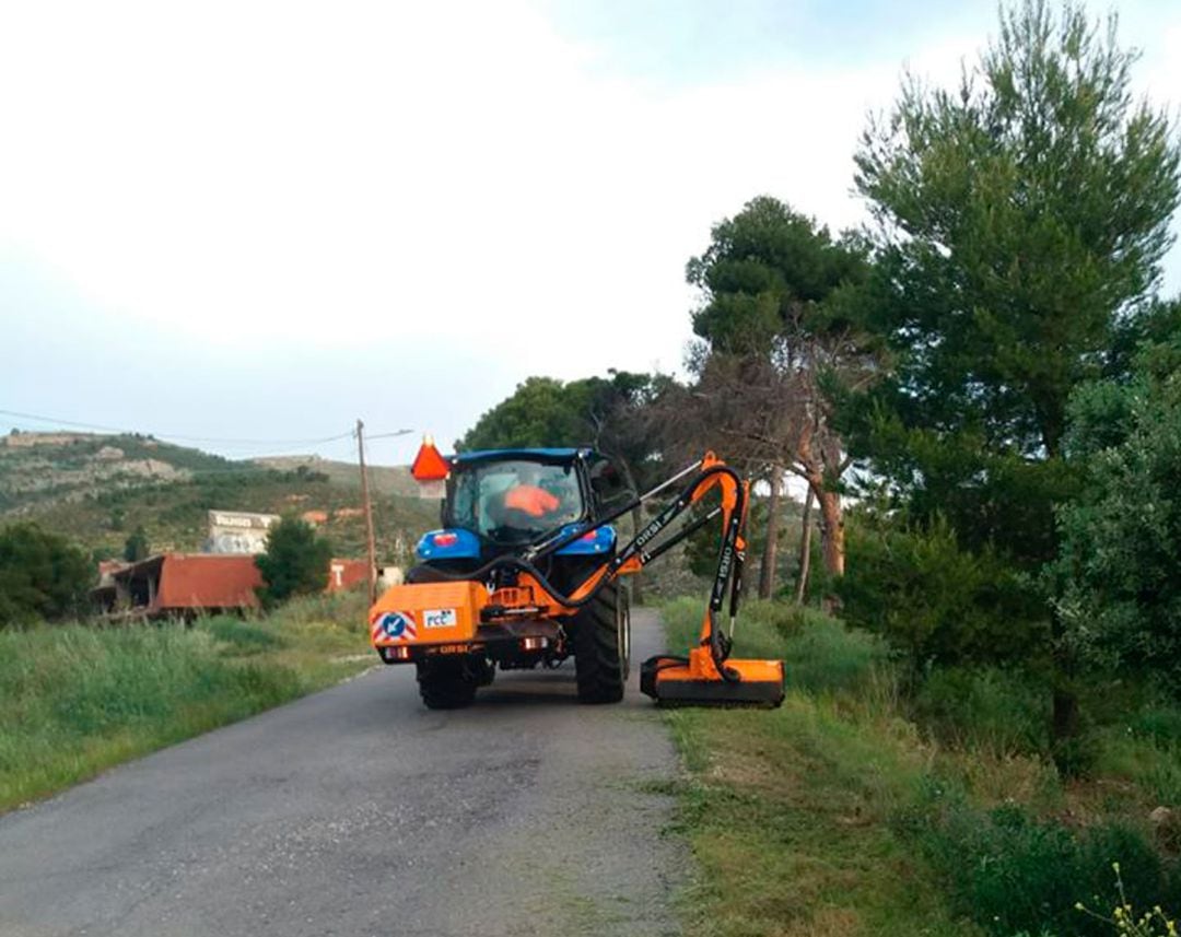 Una máquina cortando hierba en la orilla de un camino.