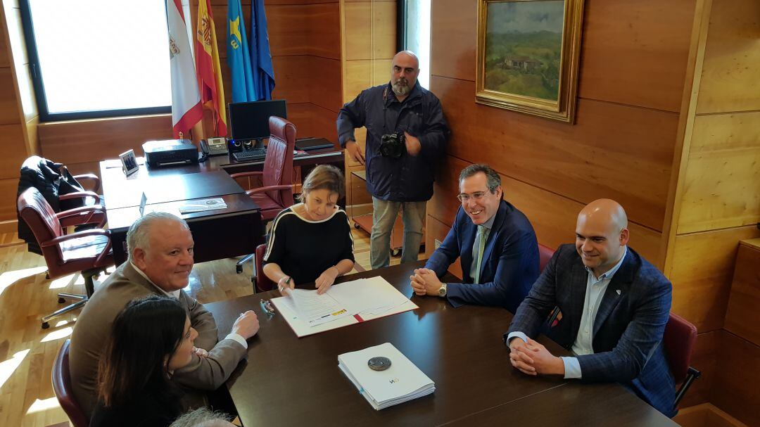 La alcaldesa, Carmen Moriyón, firma el documento del plan de vías en presencia del secretario municipal y miembros de su equipo de gobierno. 