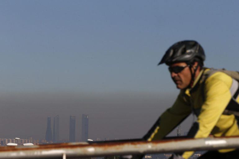 Un ciclista pasea por Pozuelo ante la vista de las Cuatro Torres de Madrid, en la que se aprecia la nube de contaminación que cubre la ciudad.