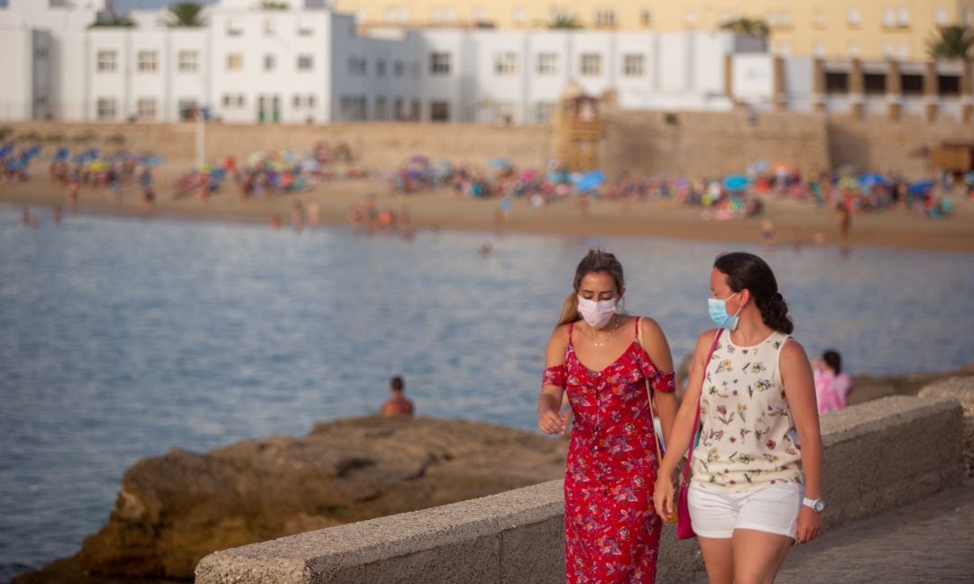 Dos mujeres paseando con mascarilla en la playa La Caleta, Cádiz.