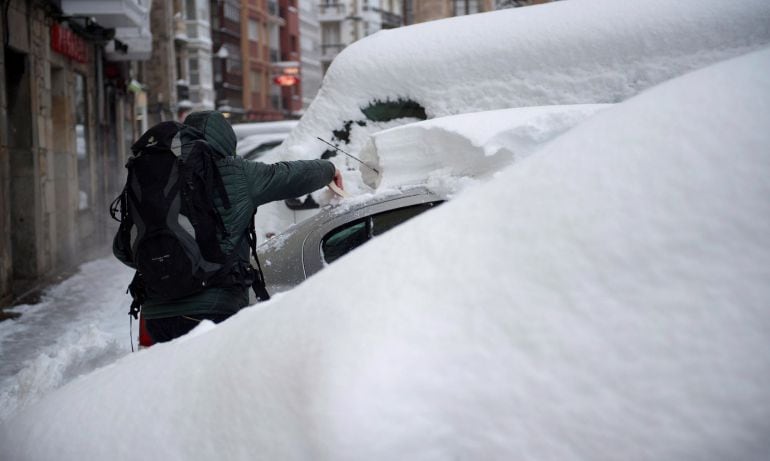 Un hombre quita la nieve de un coche en Reinosa.