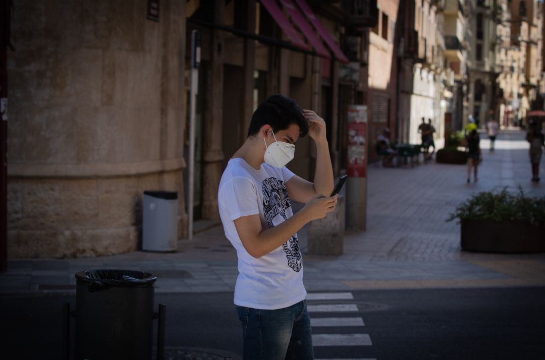 Un joven con mascarilla camina mirando el móvil.