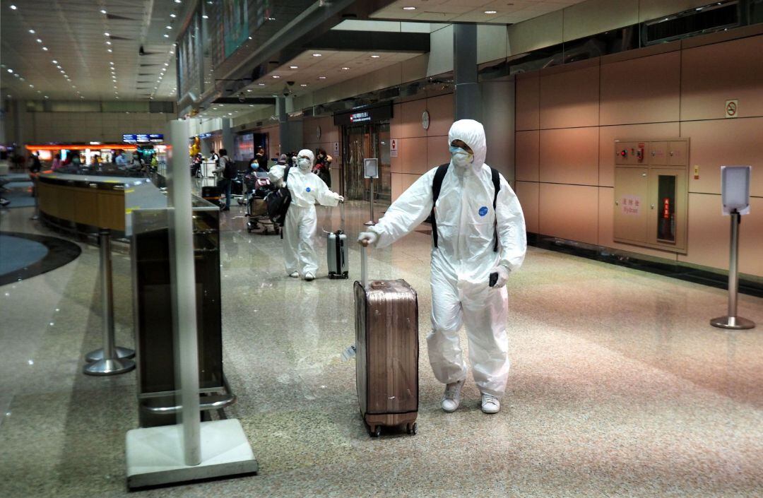 Un hombre y una mujer, vestidos con batas protectoras, llegan al aeropuerto internacional de Taoyuan en Taoyuan, norte de Taiwán.