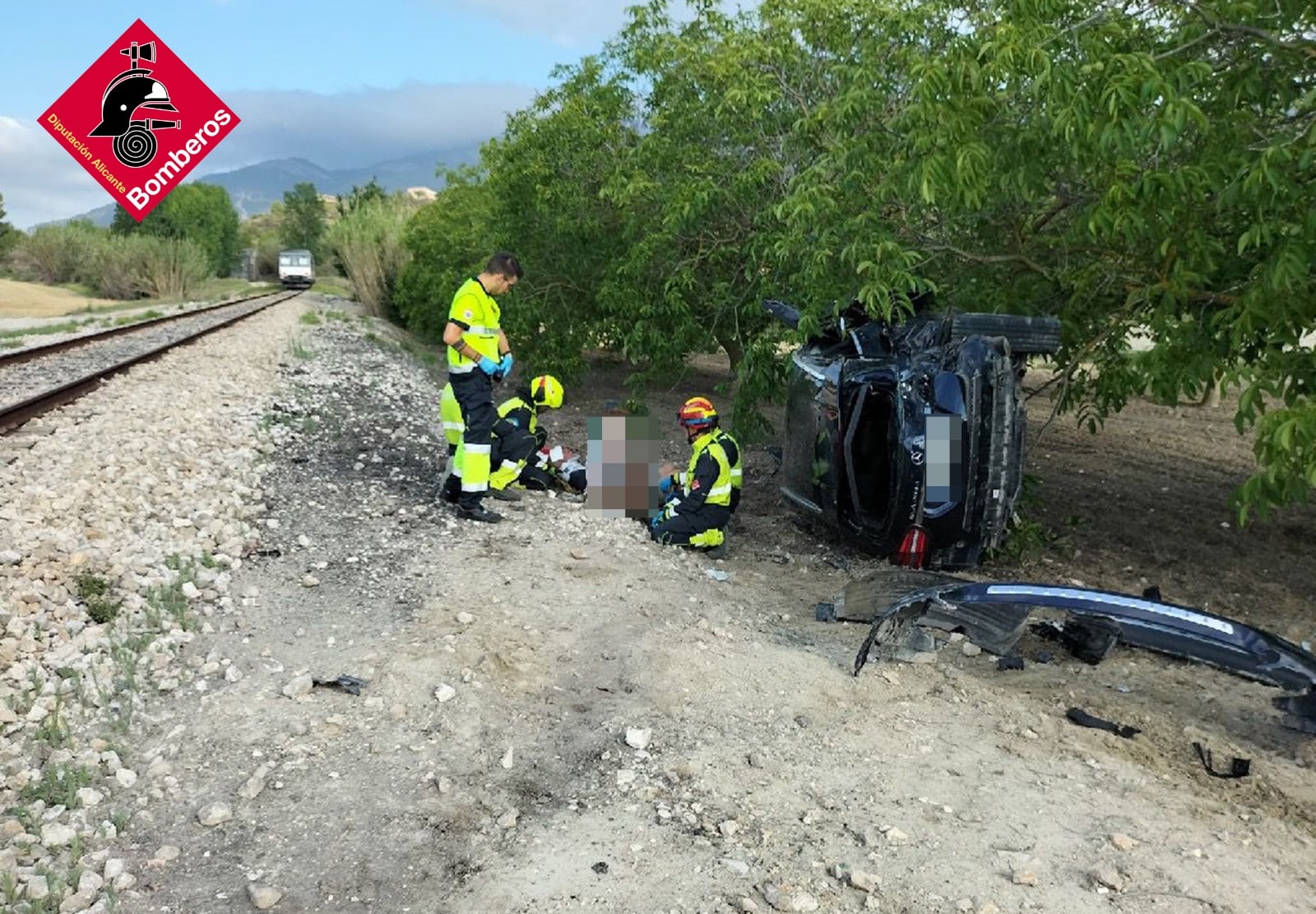 El personal sanitario y los bomberos del parque de la Muntanya atendiendo a los dos heridos tras el choque entre el tren y un automóvil en un paso a nivel en Agres, de la línea Alcoi-Xàtiva.