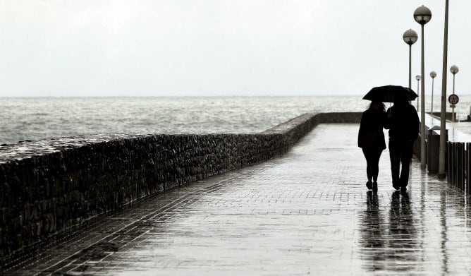 Una pareja camina por el paseo de La Zurriola de San Sebastián a pesar de que las constantes precipitaciones