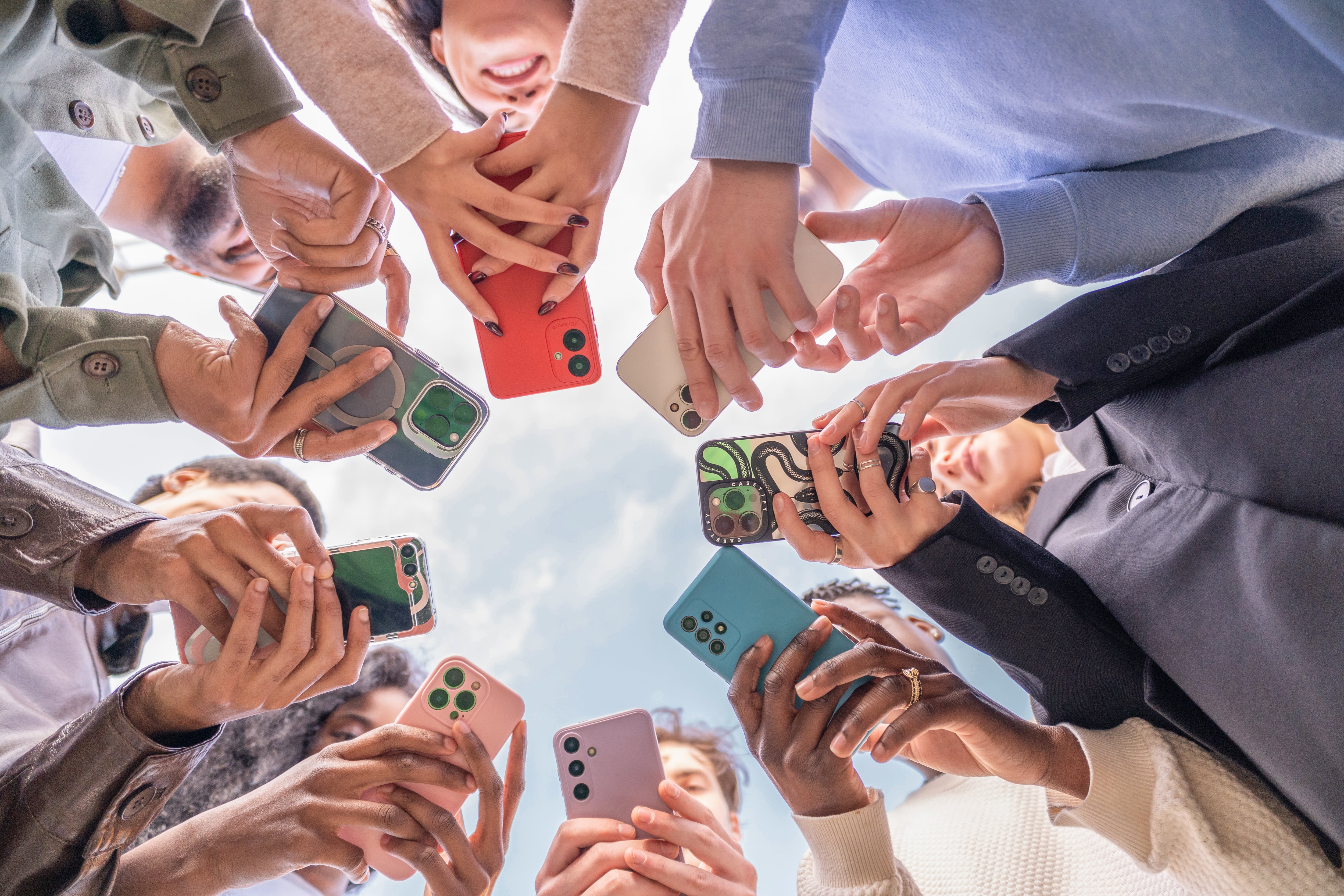 Group of young people using smartphones, forming a circle and looking down at their devices