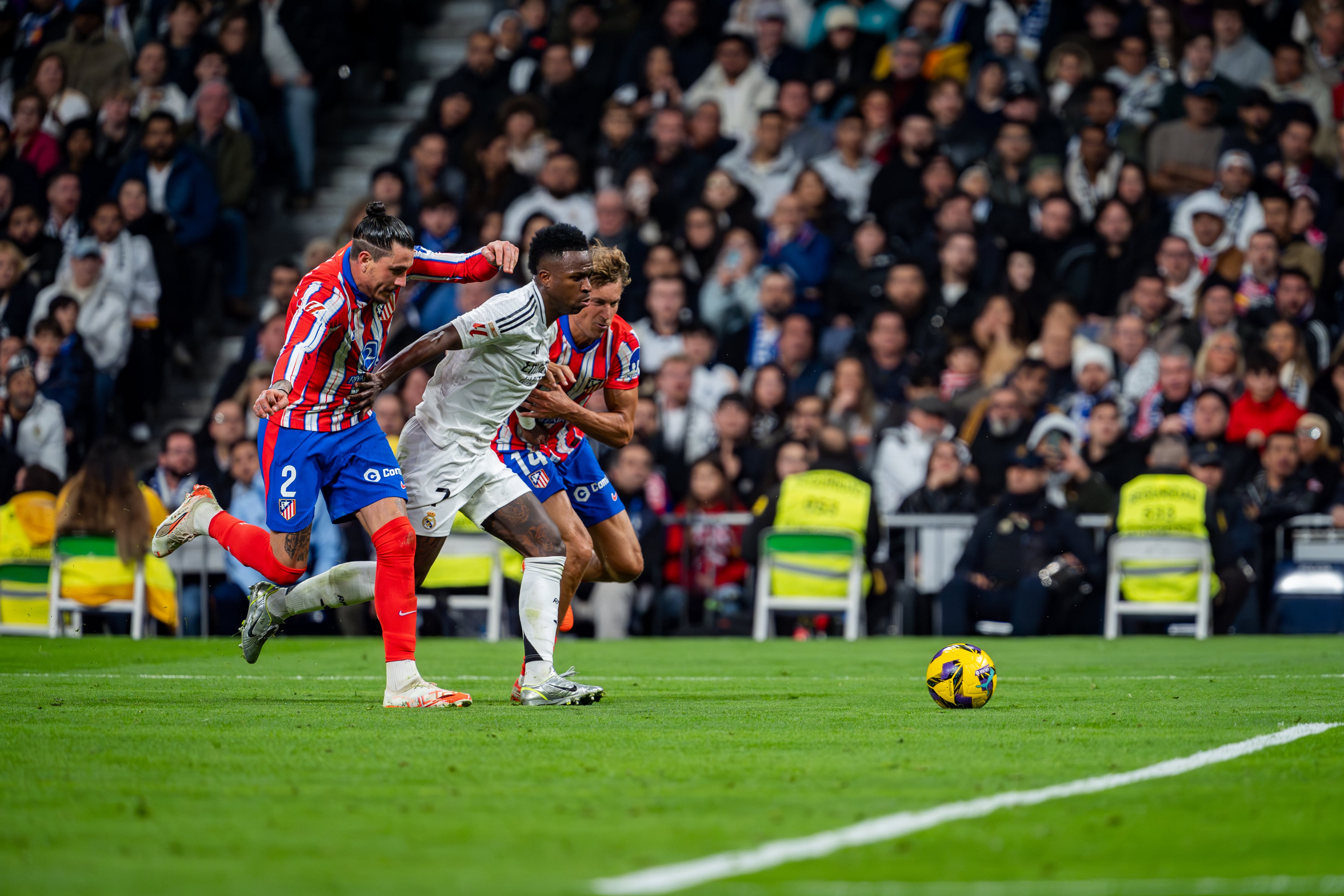 Vinicius Júnior intenta rematar a portería con la oposición de José Giménez y Marcos Llorente en el pasado Madrid-Atlético de Liga