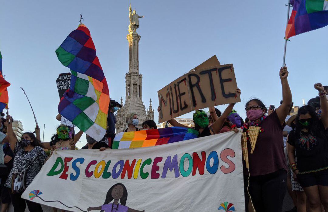 Un grupo de manifestantes frente a la estatua de Colón en Madrid portan pancartas donde puede leerse &quot;Descolonicémonos&quot; o &quot;Las vidas indígenas importan&quot;