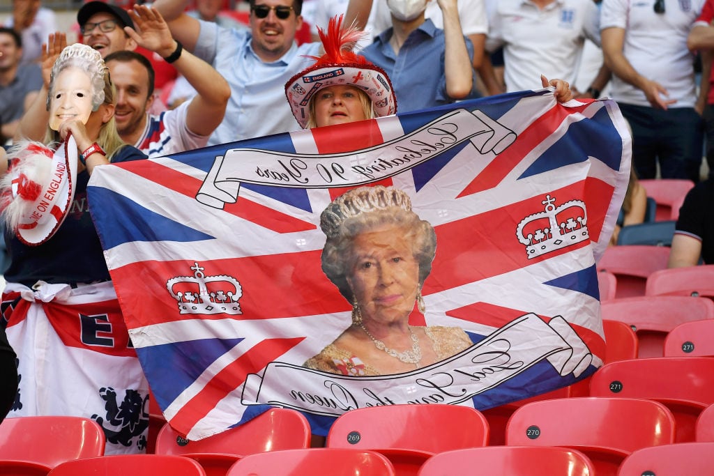 Una aficionada de fútbol sostiene una bandera con la cara de la reina Isabel II.