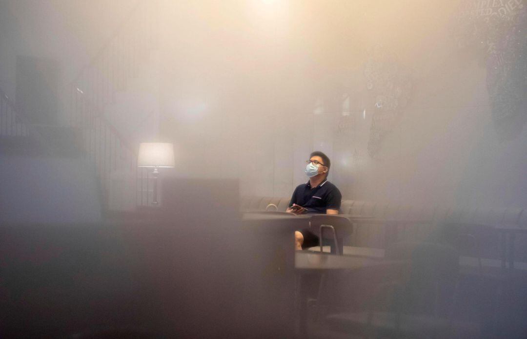 Un hombre con mascarilla sentado en un café es visto a través de una ventana empañada por la humedad en Guangzhou, provincia de Guangdong, China.