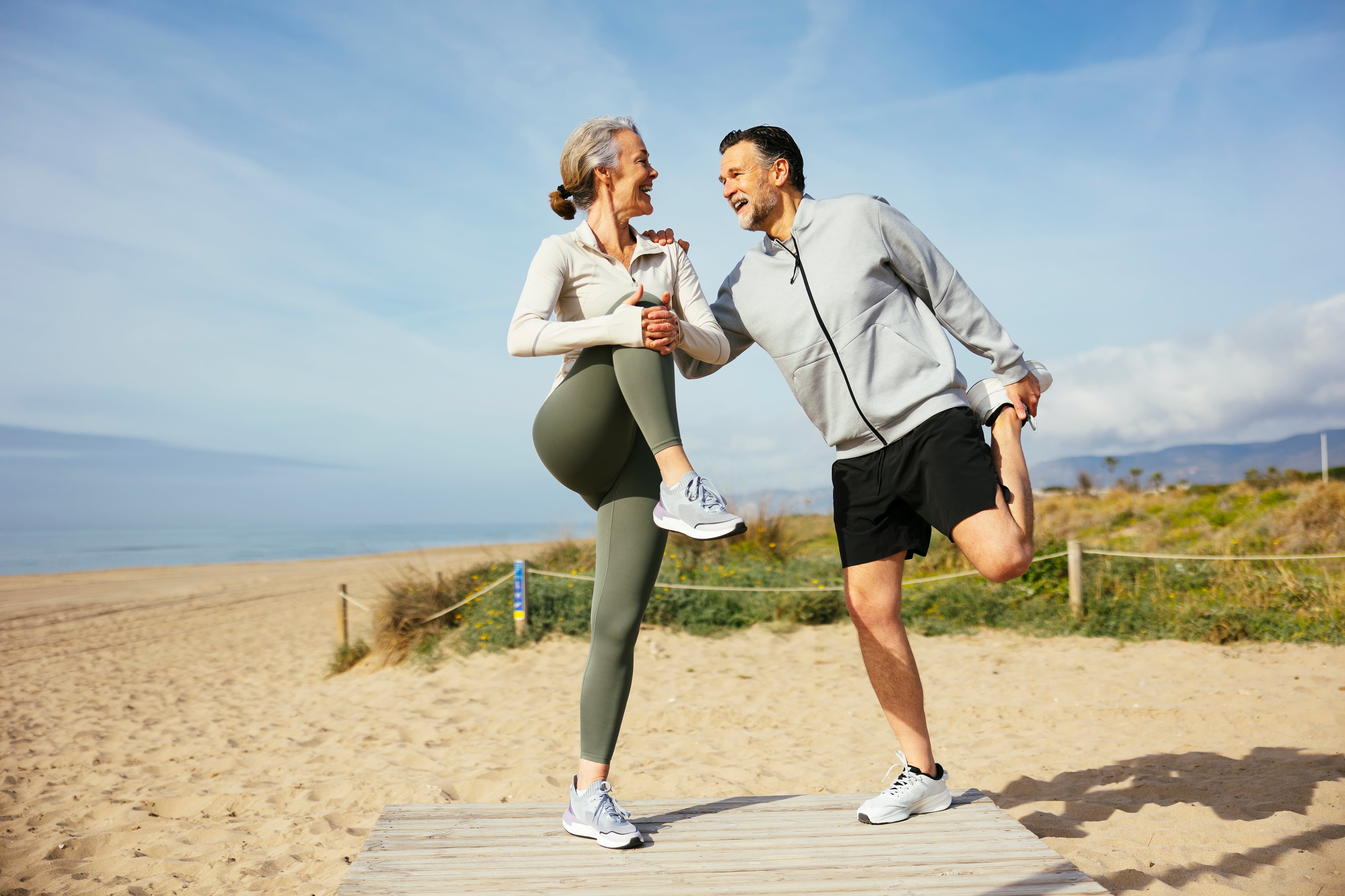 Happy mature couple stretching legs at beach