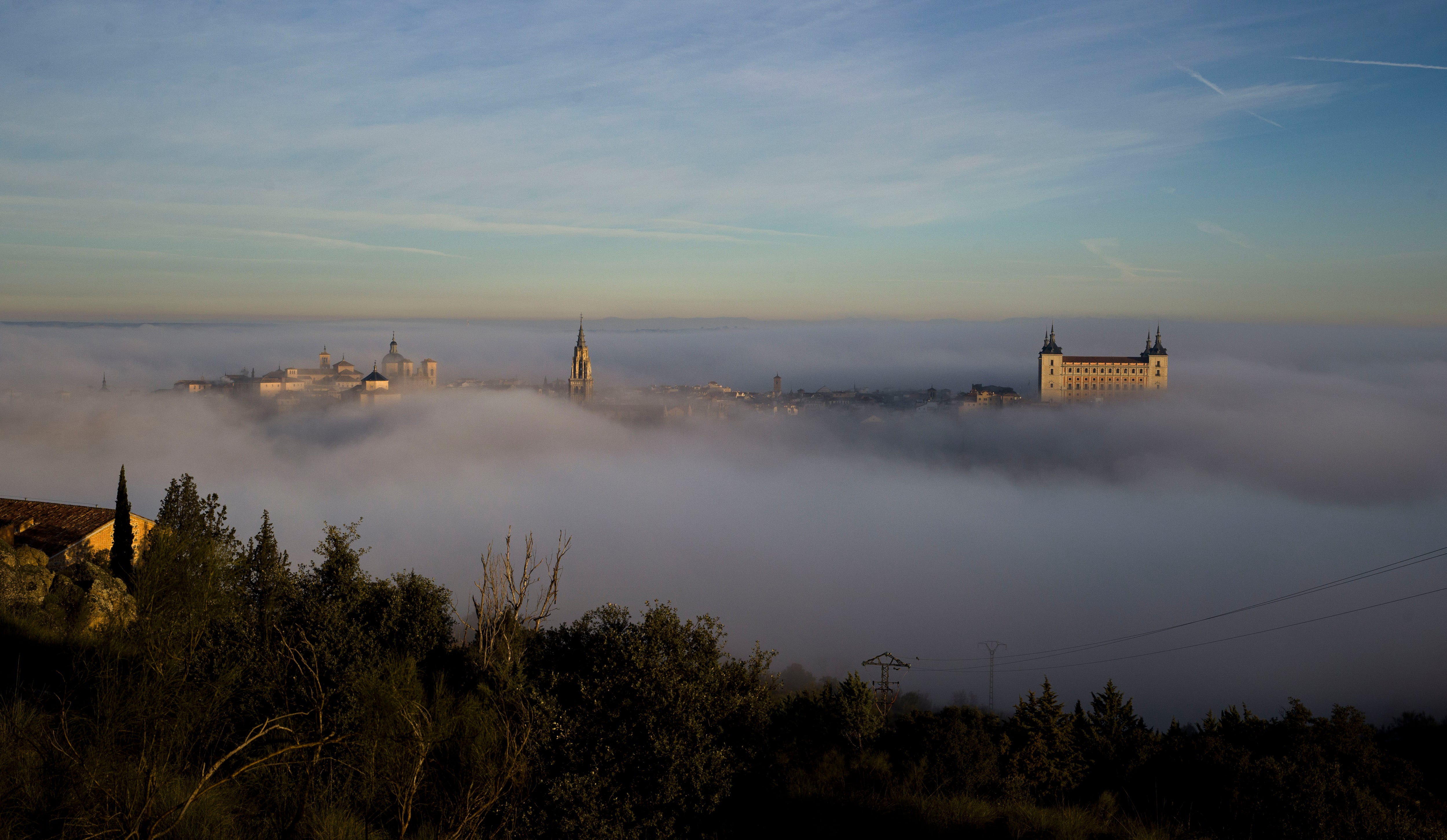 -FOTODELDIA- TOLEDO, 25/01/2024.- La niebla que cubre por completo el casco histórico de Toledo, a primera hora de la mañana, empieza a dejar ver el campanario de la catedral primada y el Alcázar de la ciudad. EFE/Ismael Herrero
