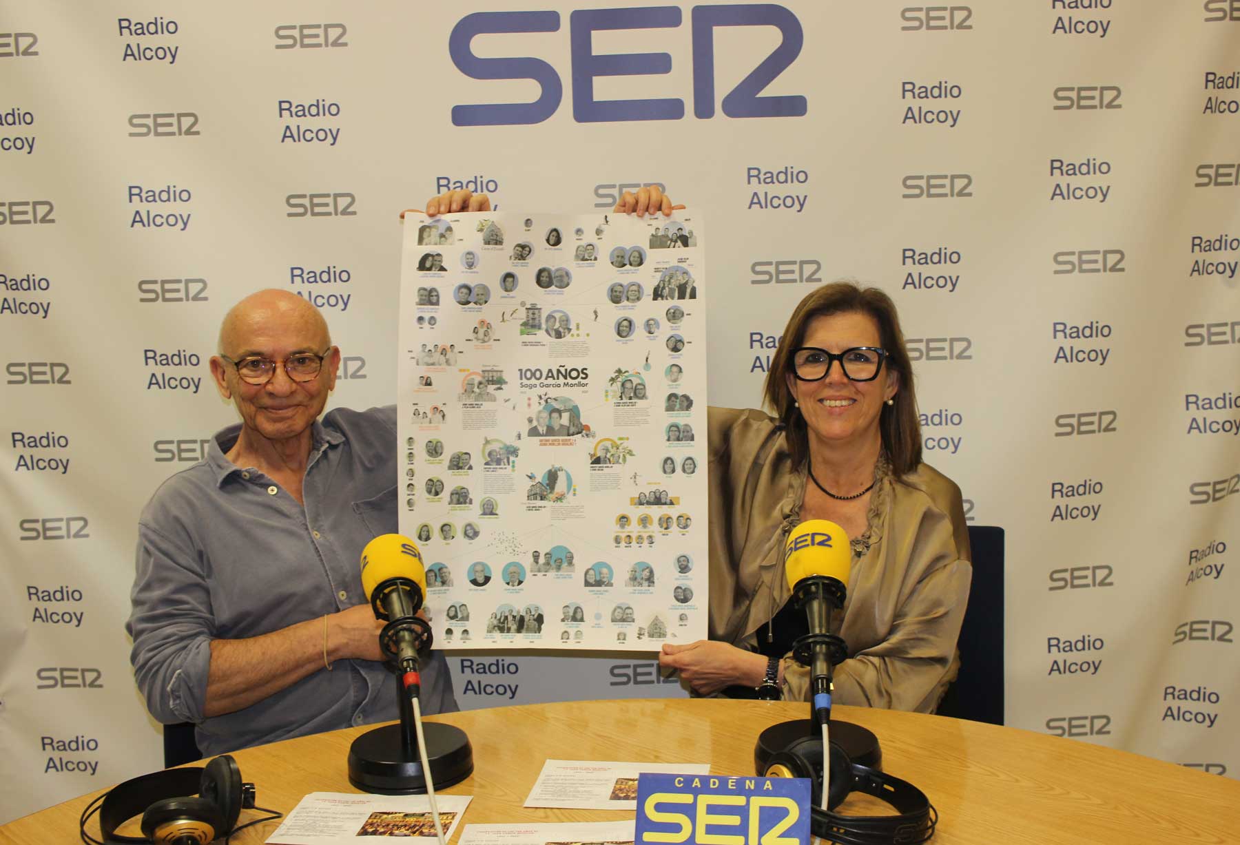 Tono Aracil y María Paula Miró, en el estudio central de Radio Alcoy sostienen un poster con el árbol genealógico de la familia