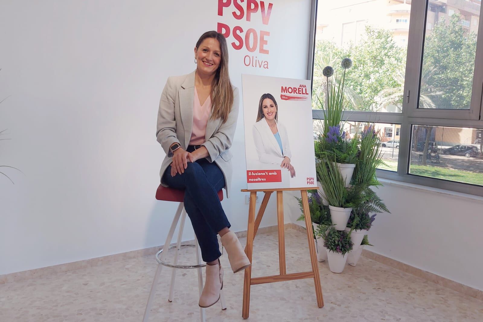 La candidata a la alcaldía de Oliva, Ana Morell, junto al cartel oficial de la campaña.