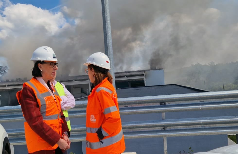 La consejera Nieves Roqueñí junto a la gerente de Cogersa, Paz Orviz, hablan sobre el incendio que, detrás de ellas, destruyó parcialmente la nave de tratamiento de la fracción resto