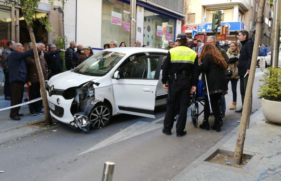 Varias personas junto al coche accidentado en la calle Rastro.