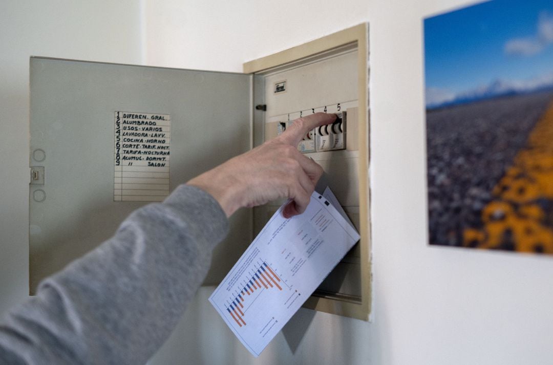 Un hombre sube los plomos de la luz con una factura de luz en la mano, a 3 de enero de 2022, en Madrid.