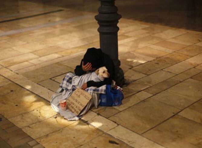 Persona que pide en la calle junto a su perro