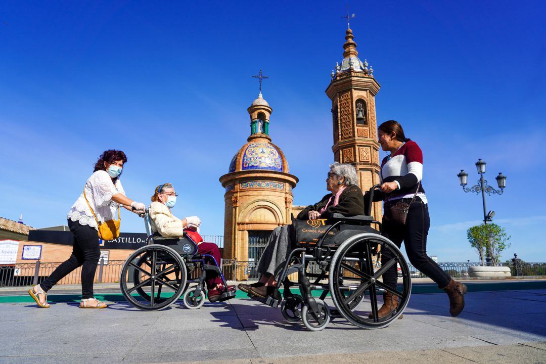 Dos personas mayores en silla de ruedas se saludan a la entrada del Puente de Triana, en Sevilla (Andalucía).