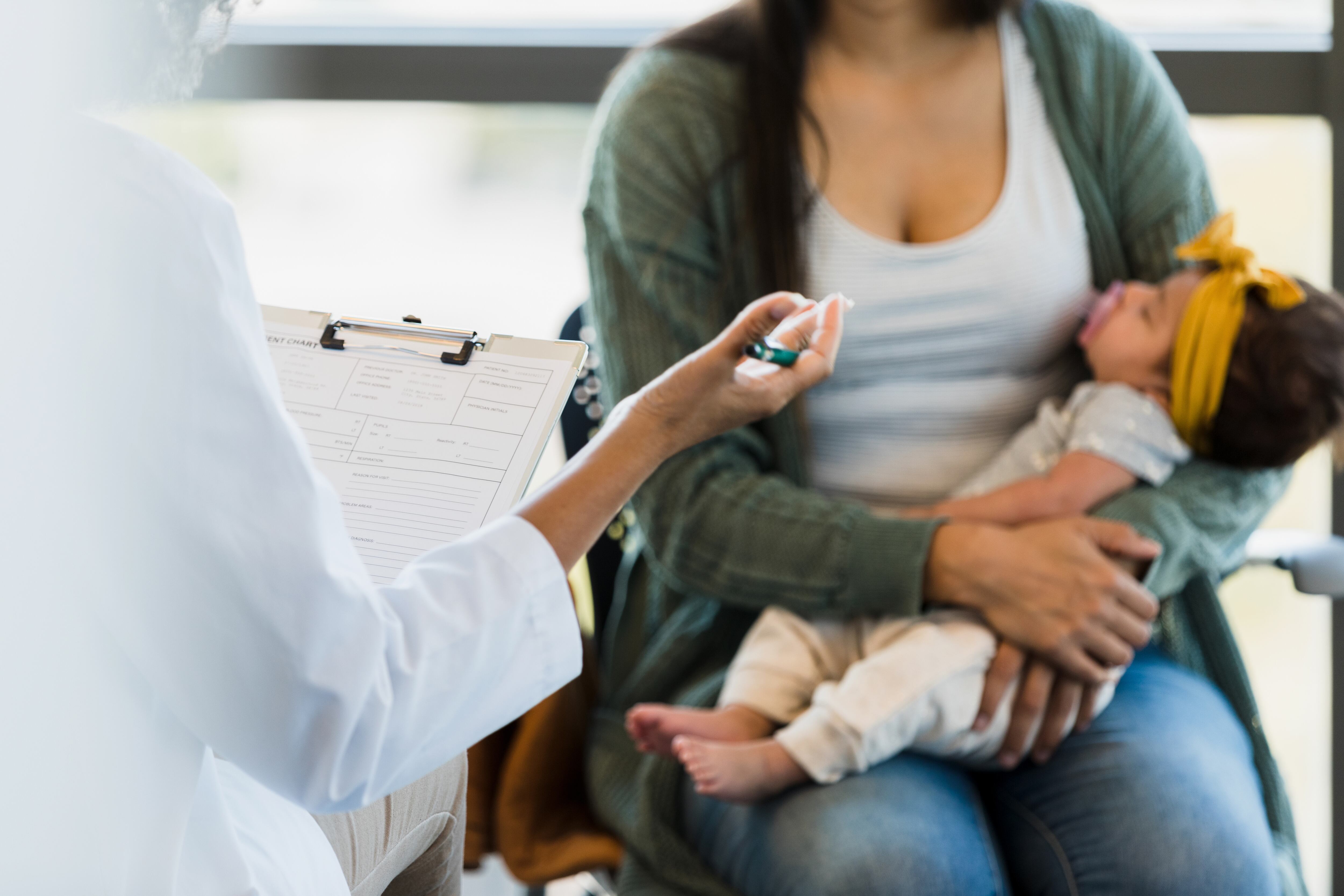 An unrecognizable female doctor gestures as she advises the mid adult mother holding the newborn baby girl.