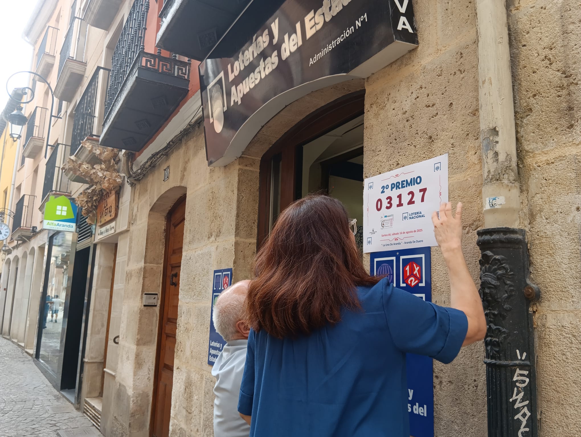 La responsable de la administración  número 1, Mercedes de Ribera Guillén, coloca en la puerta el cartel facilitado por el organismo de apuestas que acredita el premio