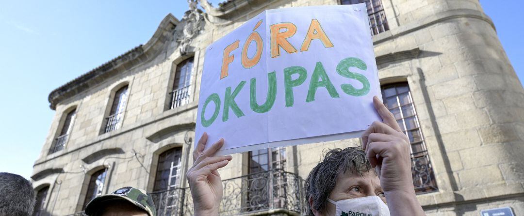 Una persona sostiene un cartel donde se puede leer &quot;Fuera okupas&quot; durante una marcha cívica para pedir la devolución de la Casa Cornide