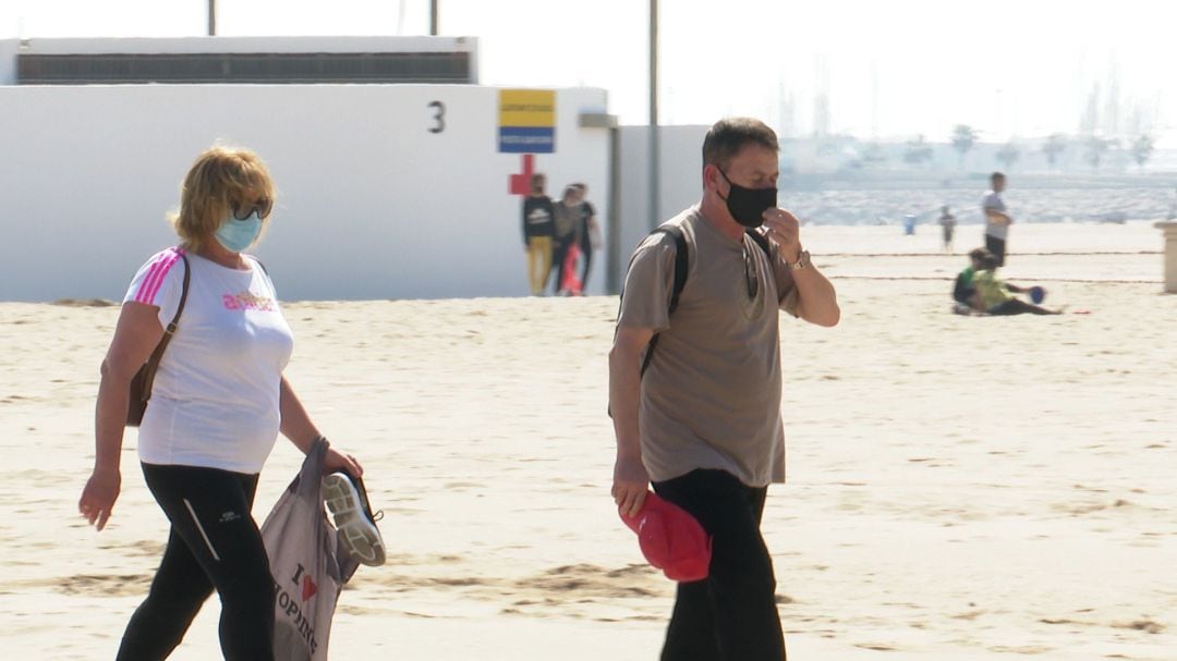 Personas con mascarilla, paseando en una playa.