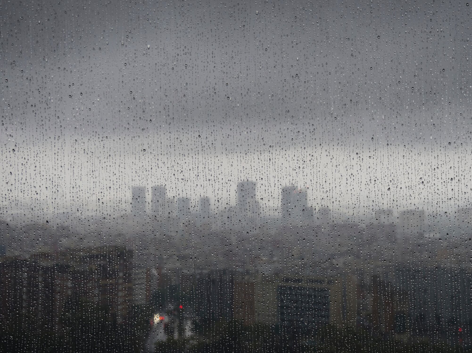 After heavy rainfall, the diffuse skyline of Barcelona is emerging in the twilight behind raindrops on a window.