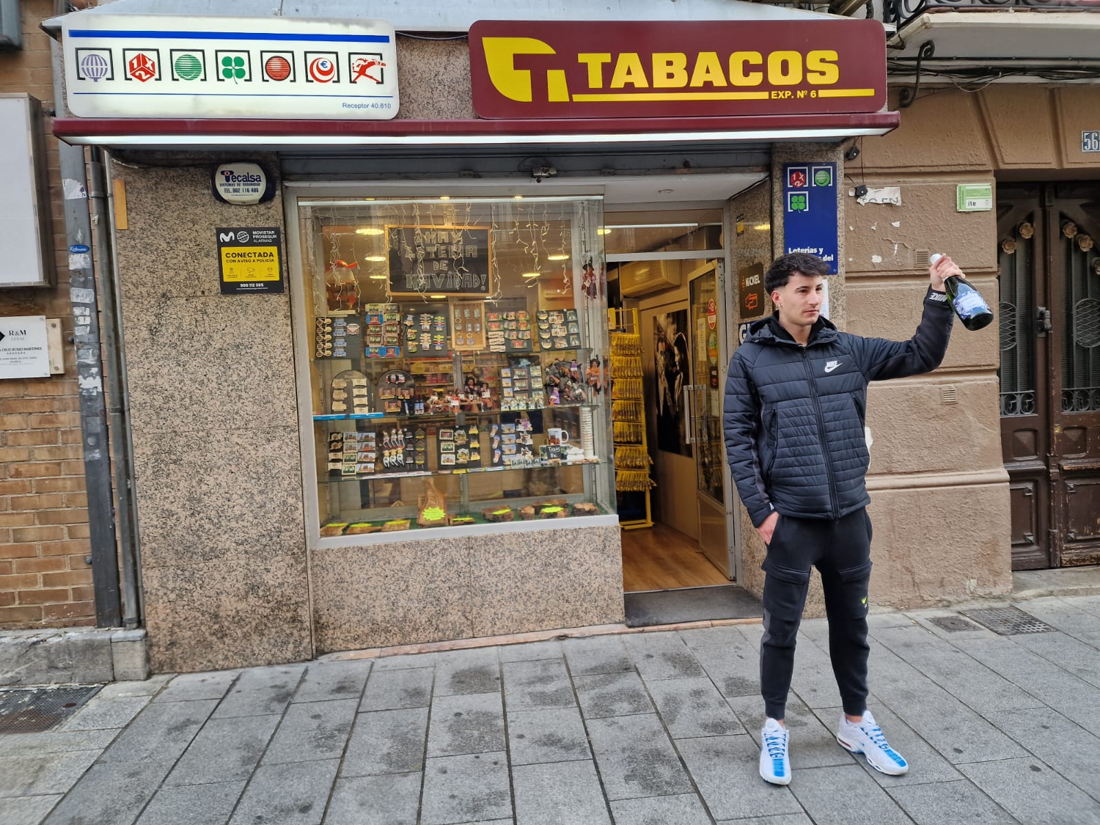 Adrián Izquierdo, con una botella de cava, a las puertas de su estanco, celebrando el 3º premio