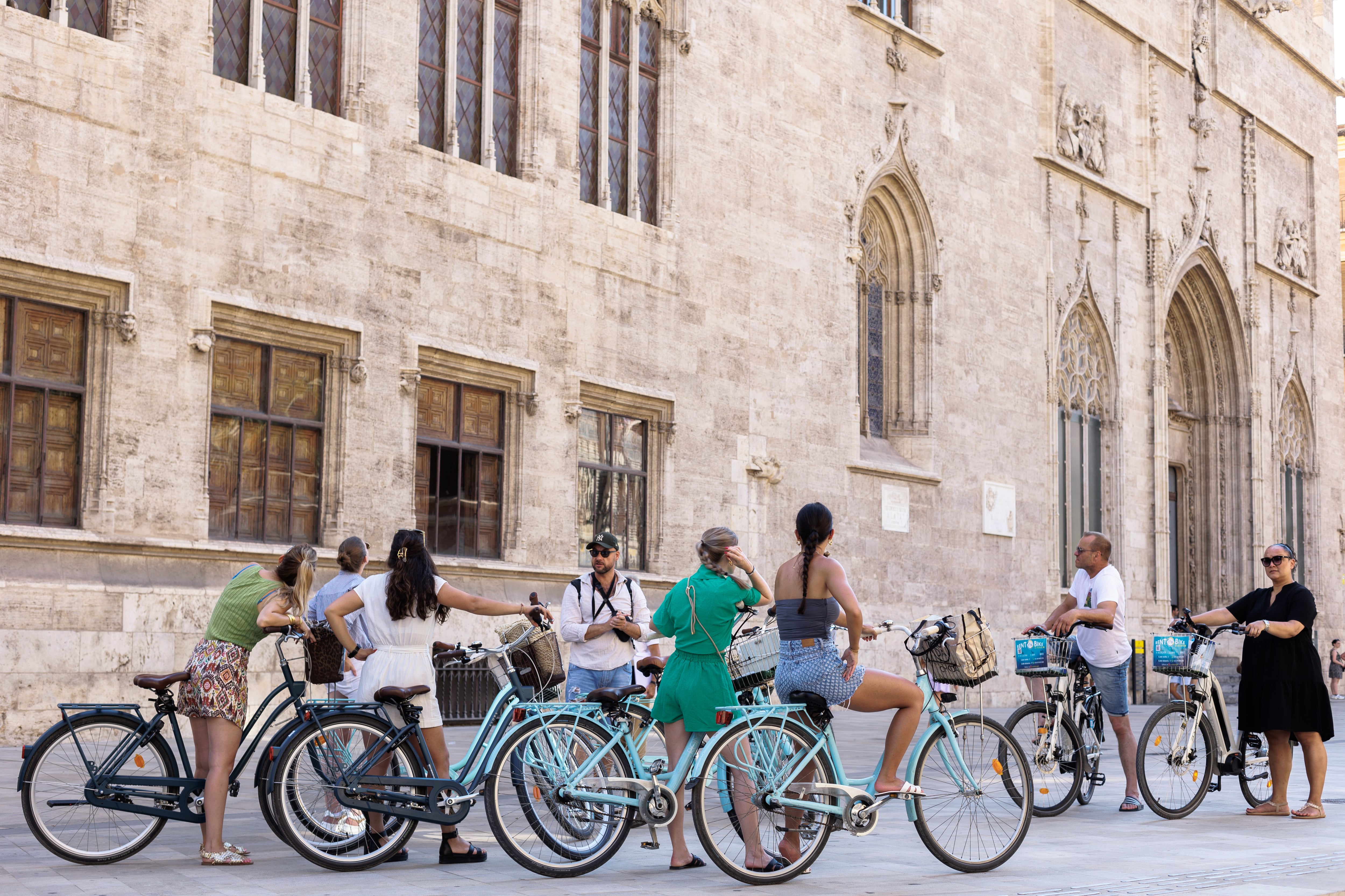 Un grupo de turistas en bicicleta escucha las explicaciones de su guía ante el edificio de La Lonja en el centro histórico de València. EFE/Biel Aliño