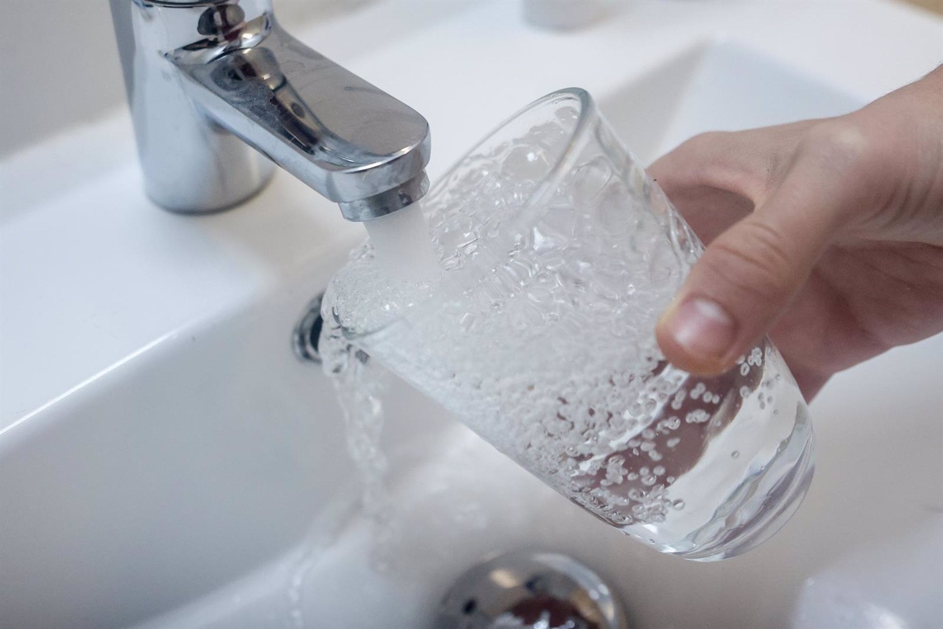 Una persona llena un vaso de agua de un grifo