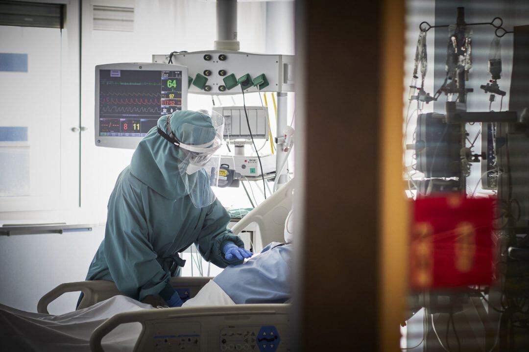 Un trabajador sanitario atiende a un paciente en una camilla de la UCI.