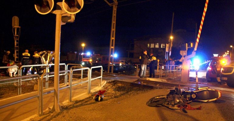 Pla general de la motocicleta on anaven els dos menors tombada al costat del pas a nivell i al fons a l'esquerra els serveis d'emergències intentant reanimar el ferit greu prop del pas a nivell de Mollerussa, el 9 de febrer de 2015.